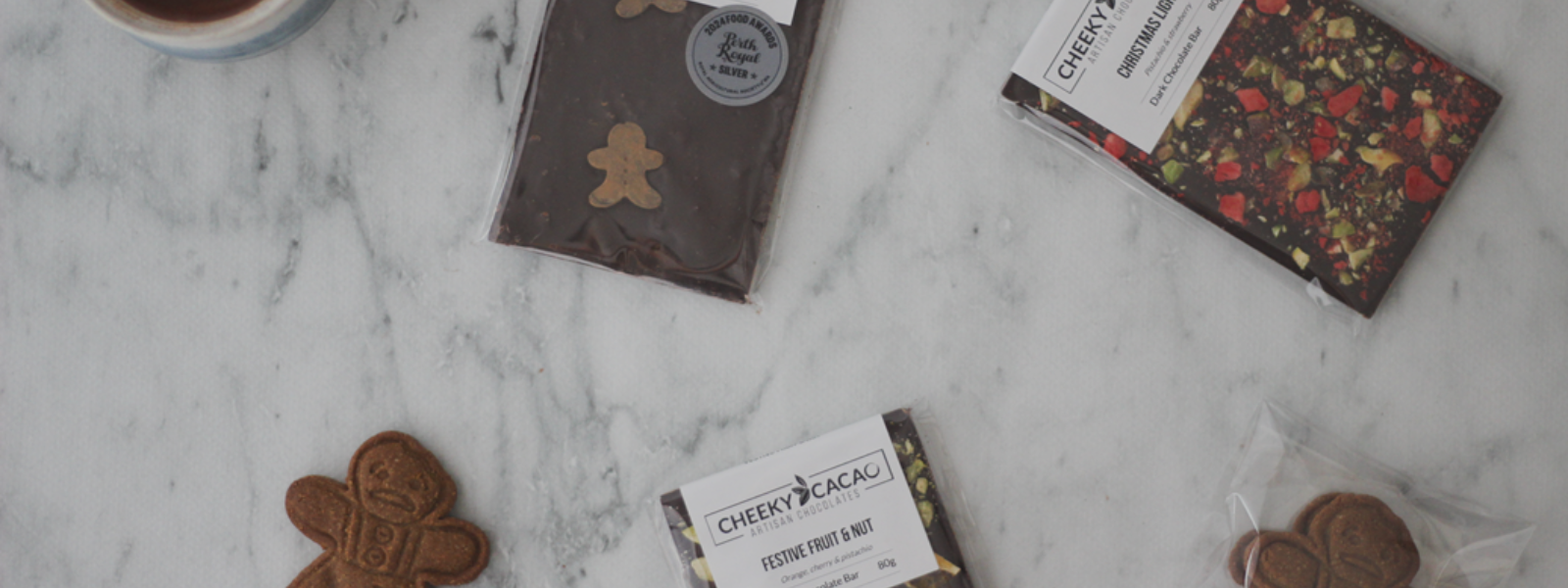 Assorted chocolate bars and cookies on a marble surface with 'Cheeky Cacao' branding.