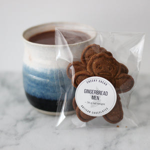 Packaged gingerbread men with a mug of hot chocolate on a marble surface